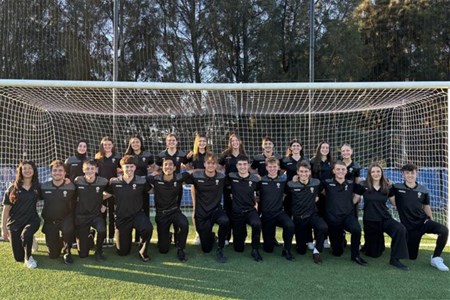 a group of people posing for a photo in front of a fence