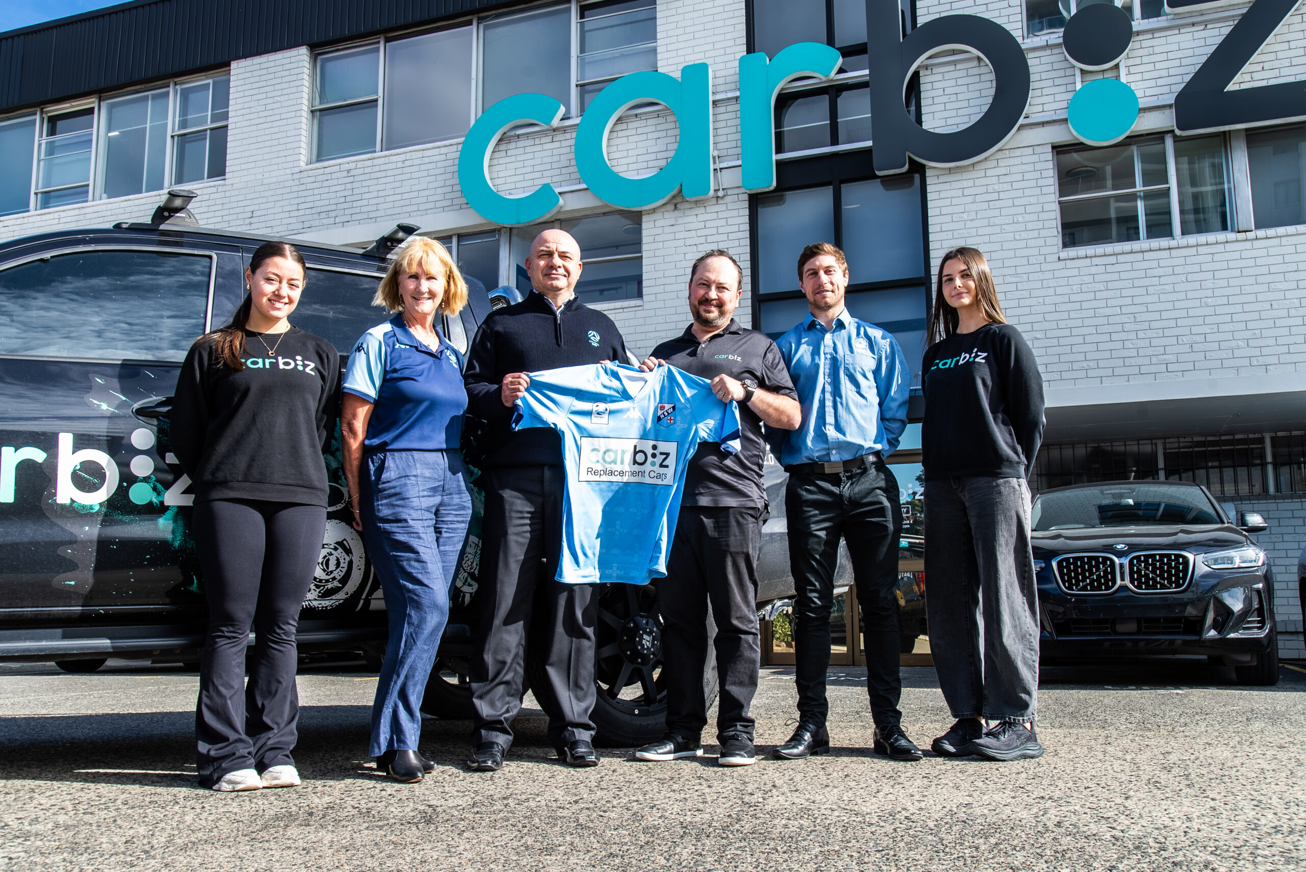 a group of people standing in front of a car posing for the camera